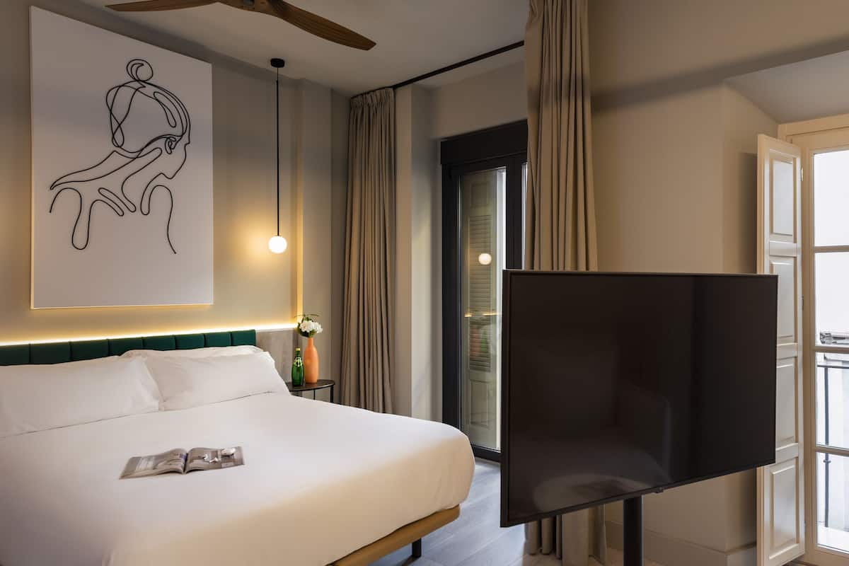Quarto de hotel com uma cama grande, televisão de tela plana, obra de arte moderna e uma janela ampla com cortinas.