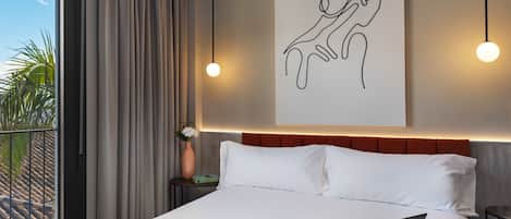 Une chambre d’hôtel moderne avec un grand lit, un ordinateur portable posé sur le lit, un magazine et une œuvre d’art murale.
