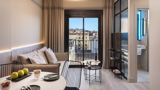 A modern living room with a sofa, dining table, and a balcony with a city view. - Coeo Peña Design Apartments (Málaga)