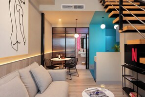 A modern living room with a sofa, a dining table with chairs, a TV stand with a Netflix logo, and a staircase. - Coeo Peña Design Apartments (Málaga)