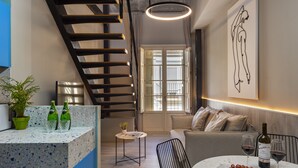 A modern kitchen with a staircase, a dining area with a table set for two, and a living room with a sofa. - Coeo Peña Design Apartments (Málaga)
