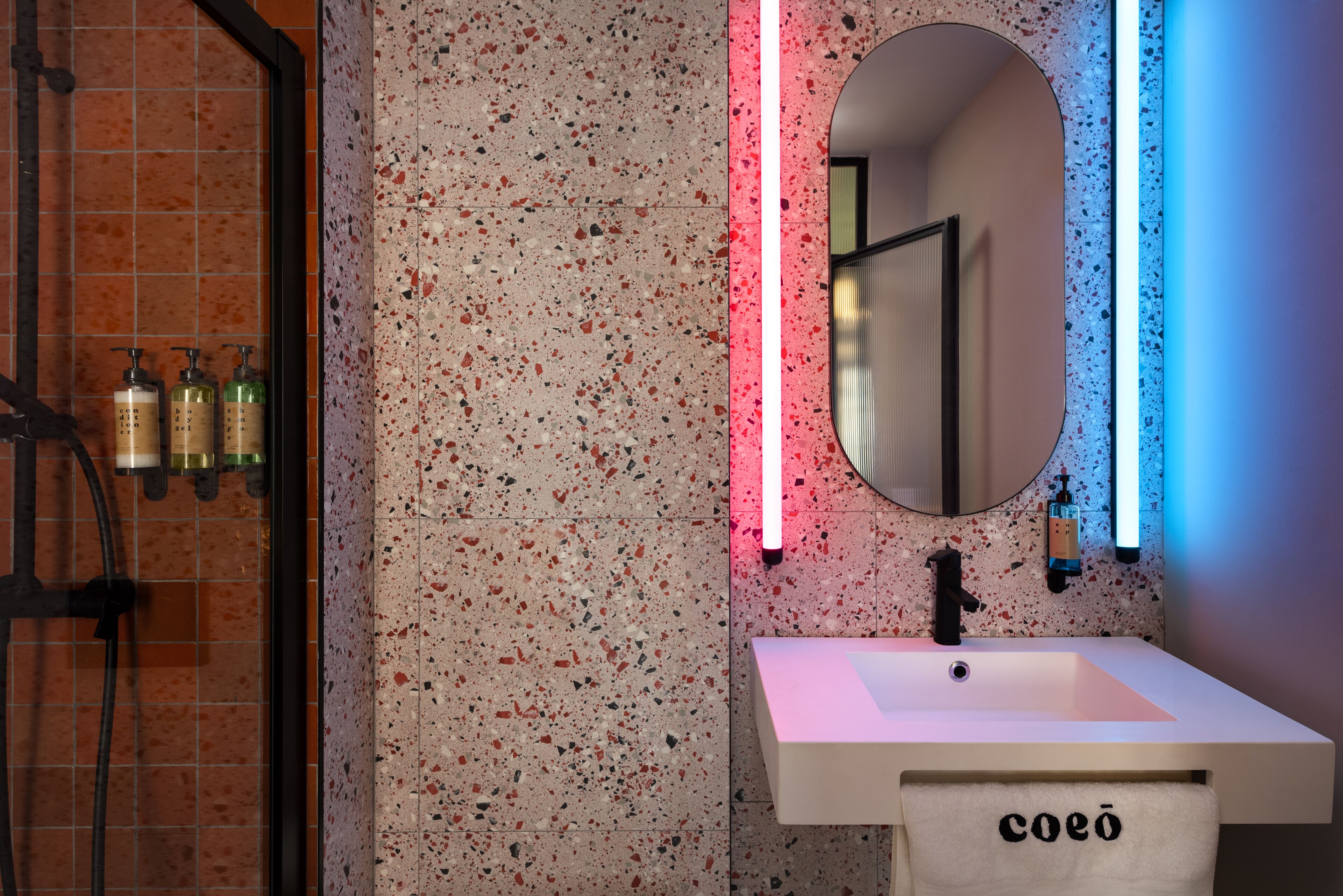 A bathroom with a white sink, a mirror, and a towel rack with a towel labeled "coeo".