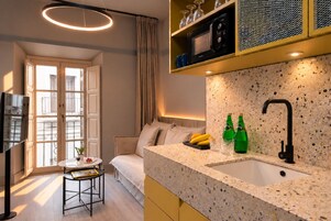 Cocina moderna con encimera de granito, pileta negra y microondas. Hay un espacio de estar con sofá y una mesita con una planta.