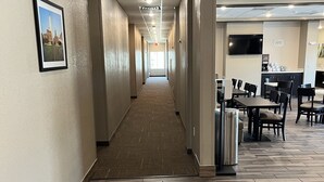 A hotel corridor with a wooden floor, a framed picture on the wall, and a seating area with tables and chairs. - MainStay Suites Dallas Northwest - Irving (Dallas)
