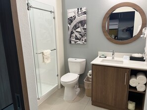 A modern bathroom with a glass shower enclosure, a white toilet, a wooden vanity with a sink, and a mirror. - MainStay Suites Dallas Northwest - Irving (Dallas)