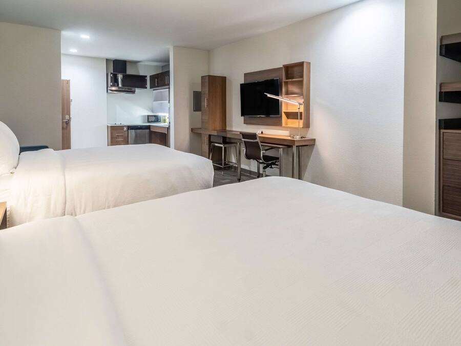 A hotel room with two beds, a desk with a chair, a TV, and a kitchenette.