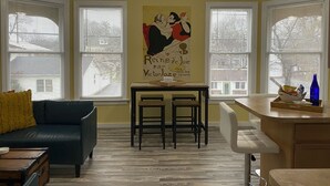 A living room with a dark blue sofa, a small table with a yellow pillow, and a poster on the wall.