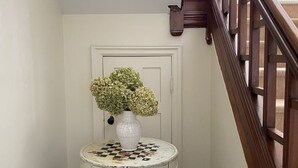 A hallway with a white door, a small round table with a checkered top, and a vase of flowers.