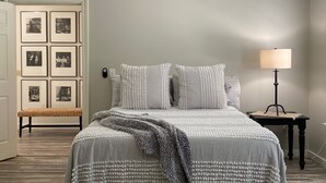 A bedroom with a bed, a ceiling fan, a bedside table with a lamp, and framed pictures on the wall.