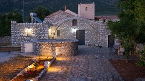 Una casa de pedra amb un pati circular, un dipòsit d'aigua a la teulada i un jardí petit amb flors.