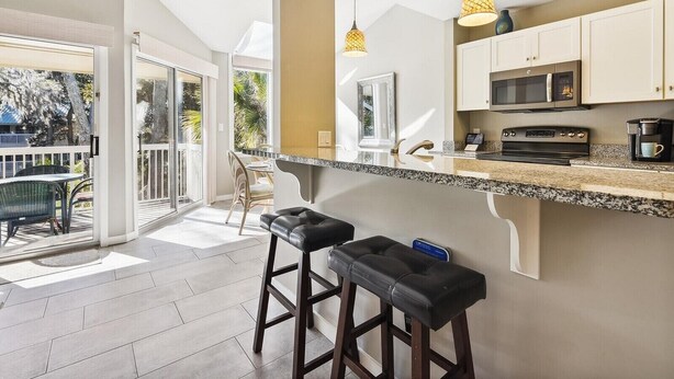 Une cuisine moderne dotée d’un grand îlot central, d’appareils électroménagers en acier inoxydable et de luminaires suspendus.