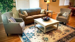 Ein Wohnzimmer mit einem braunen Sofa, gemusterten Sesseln, einem Couchtisch und einem dekorativen Teppich.