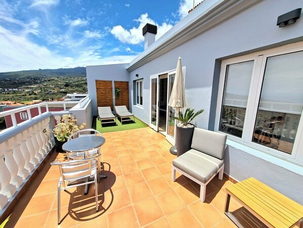 A terrace with a table and chairs, a sofa, and a potted plant.