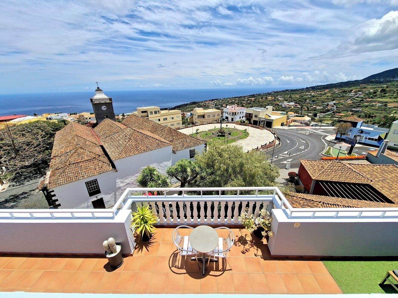 Una terraza con mesa y sillas, con vista a un pueblo costero con edificios y una carretera.