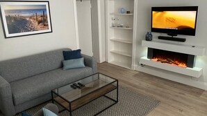 A modern living room with a grey sofa, a glass coffee table, a fireplace, and a flat-screen TV on a white shelf. - Relax by the Sea (Weymouth)