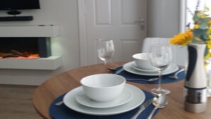 A dining table set with white plates, bowls, and cutlery, a wine glass, and a thermos. - Relax by the Sea (Weymouth)