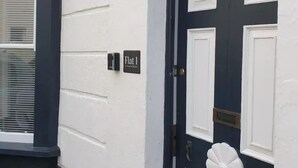 A dark blue door with white panels and a white flower-shaped knocker. A small sign above the door reads "Flat 1." - Relax by the Sea (Weymouth)