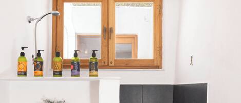 A bathroom with a wooden vanity, a shower with black tiles, and toiletries on the shelf.