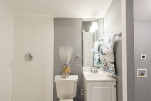 Une salle de bain avec des toilettes, un lavabo et un miroir. Un vase décoratif est posé sur les toilettes, et des serviettes sont accrochées au mur.