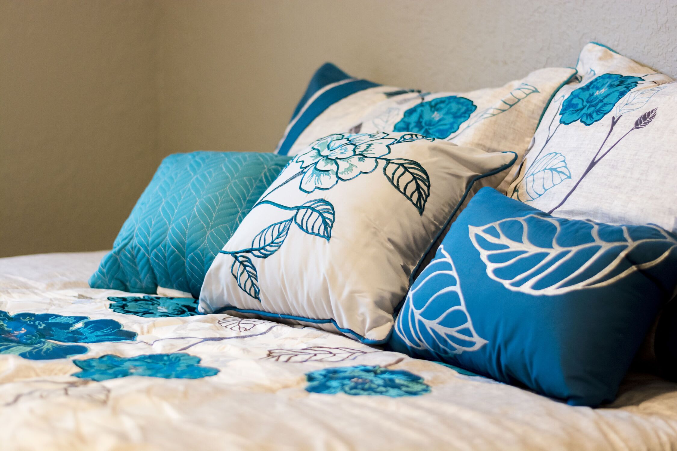 Un lit recouvert d’une couvre-lit à motifs floraux et agrémenté de plusieurs coussins aux motifs bleus et blancs.