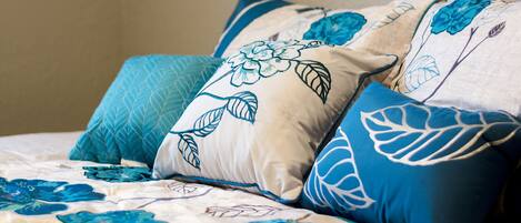 Un lit recouvert d’une couvre-lit à motifs floraux et agrémenté de plusieurs coussins aux motifs bleus et blancs.