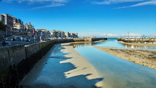 Une promenade en bord de mer, avec un large sentier, une mer calme et des bâtiments qui bordent la côte.