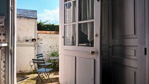 Une porte ouverte donne sur un petit patio extérieur, où se trouvent une table et des chaises.