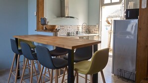 Une cuisine avec une table en bois et quatre chaises, un réfrigérateur en acier inoxydable et une fenêtre donnant sur l’extérieur.