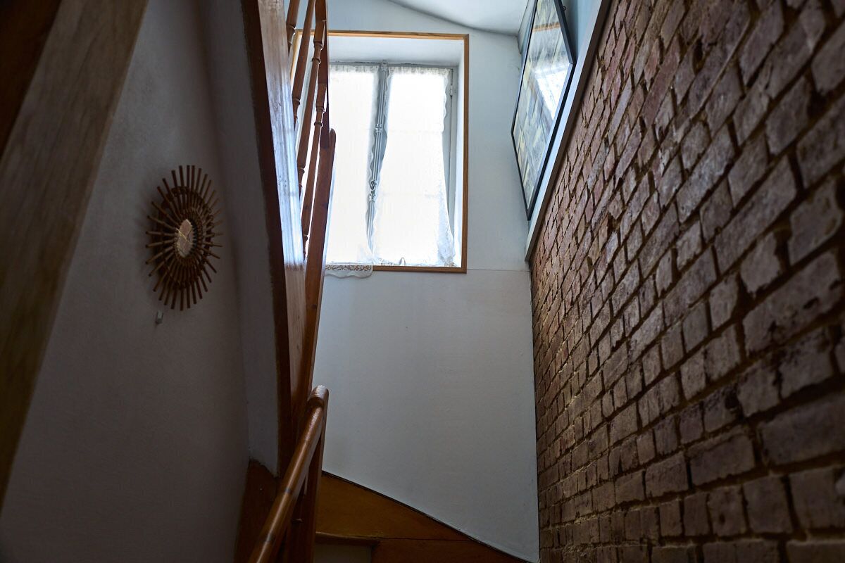 Eine Treppe mit Holzgeländer, einer Wanddekoration mit Sonnenmotiv und einem Fenster mit durchscheinenden Vorhängen.