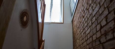 Eine Treppe mit Holzgeländer, einer Wanddekoration mit Sonnenmotiv und einem Fenster mit durchscheinenden Vorhängen.