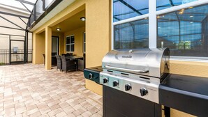 Eine Terrassenanlage im Freien mit integriertem Grill, einer Glaskonstruktion und einer Sitzgruppe.