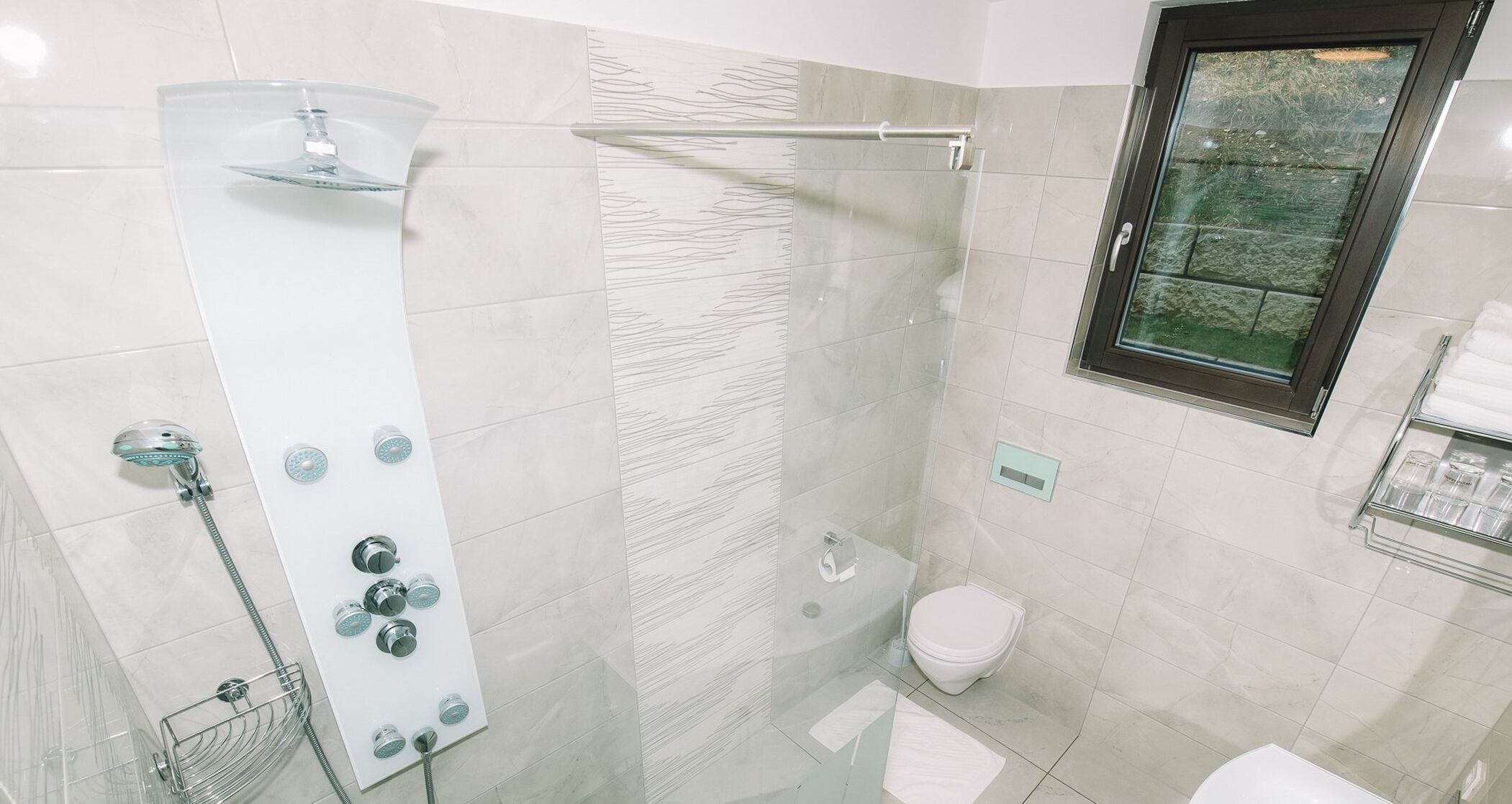 A modern bathroom with a glass shower enclosure, a toilet, and a window.