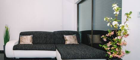 A modern living room with a sectional sofa, a potted plant, and a large window.