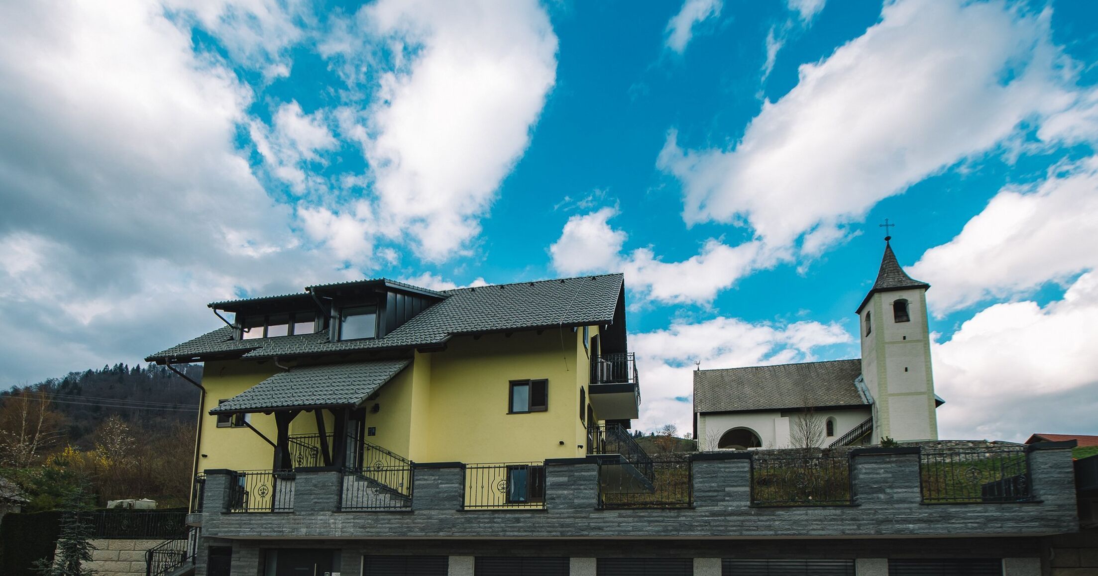A yellow building with a balcony and a church with a bell tower.