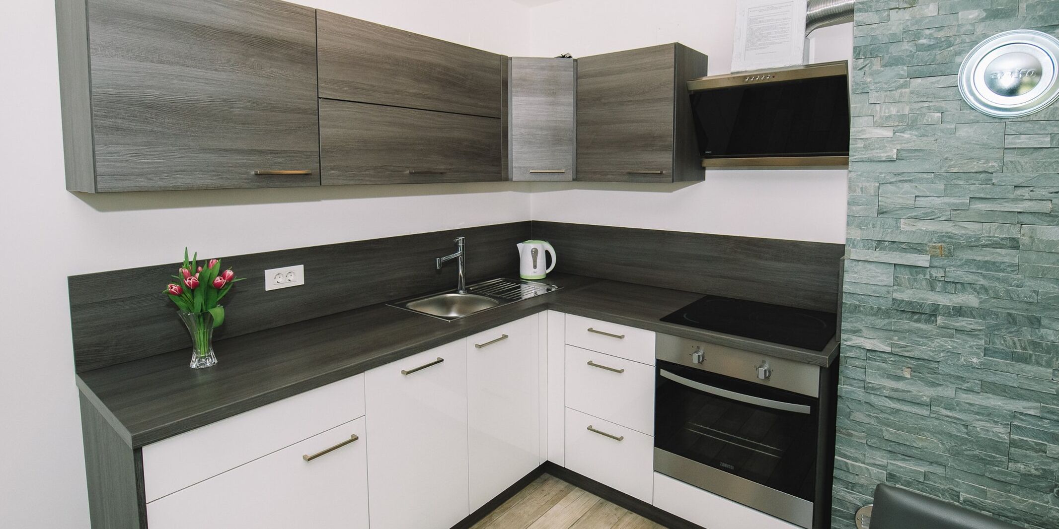 Uma cozinha moderna com bancadas escuras, armários brancos e forno embutido.
