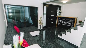 A modern reception area with a black reception desk, a glass door, and a grey sofa with red cushions.