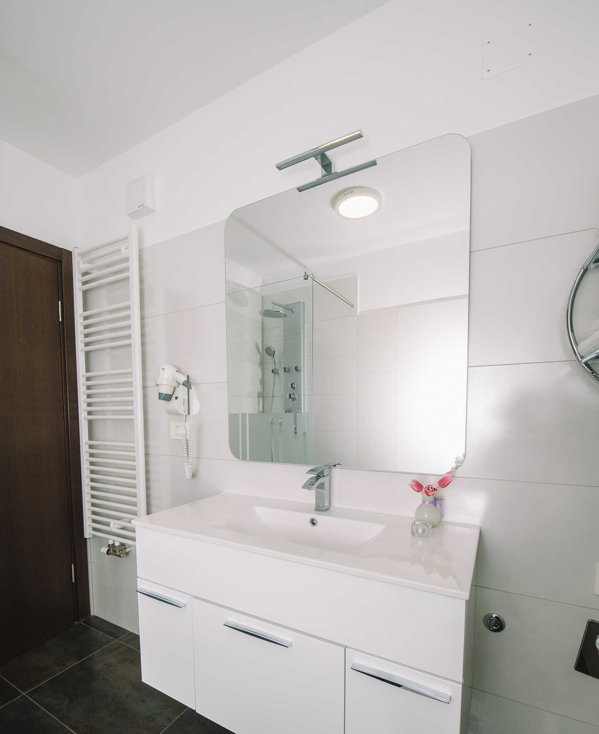 A modern bathroom with a white vanity, a large mirror, a shower, and a towel rack.