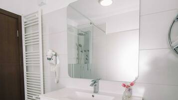 A modern bathroom with a white vanity, a large mirror, a shower, and a towel rack.