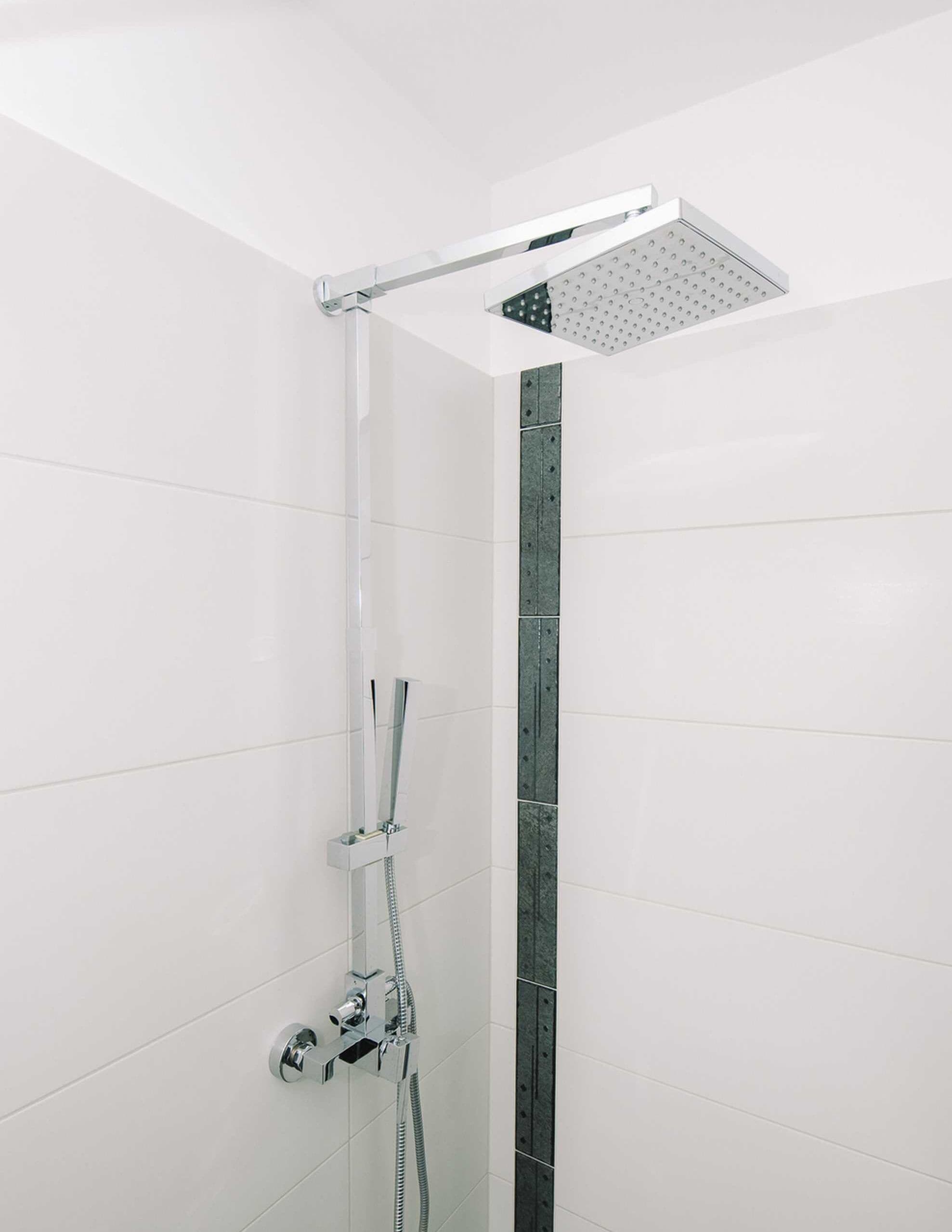 A modern shower with a rain showerhead and handheld showerhead, chrome fixtures, and a tiled wall.