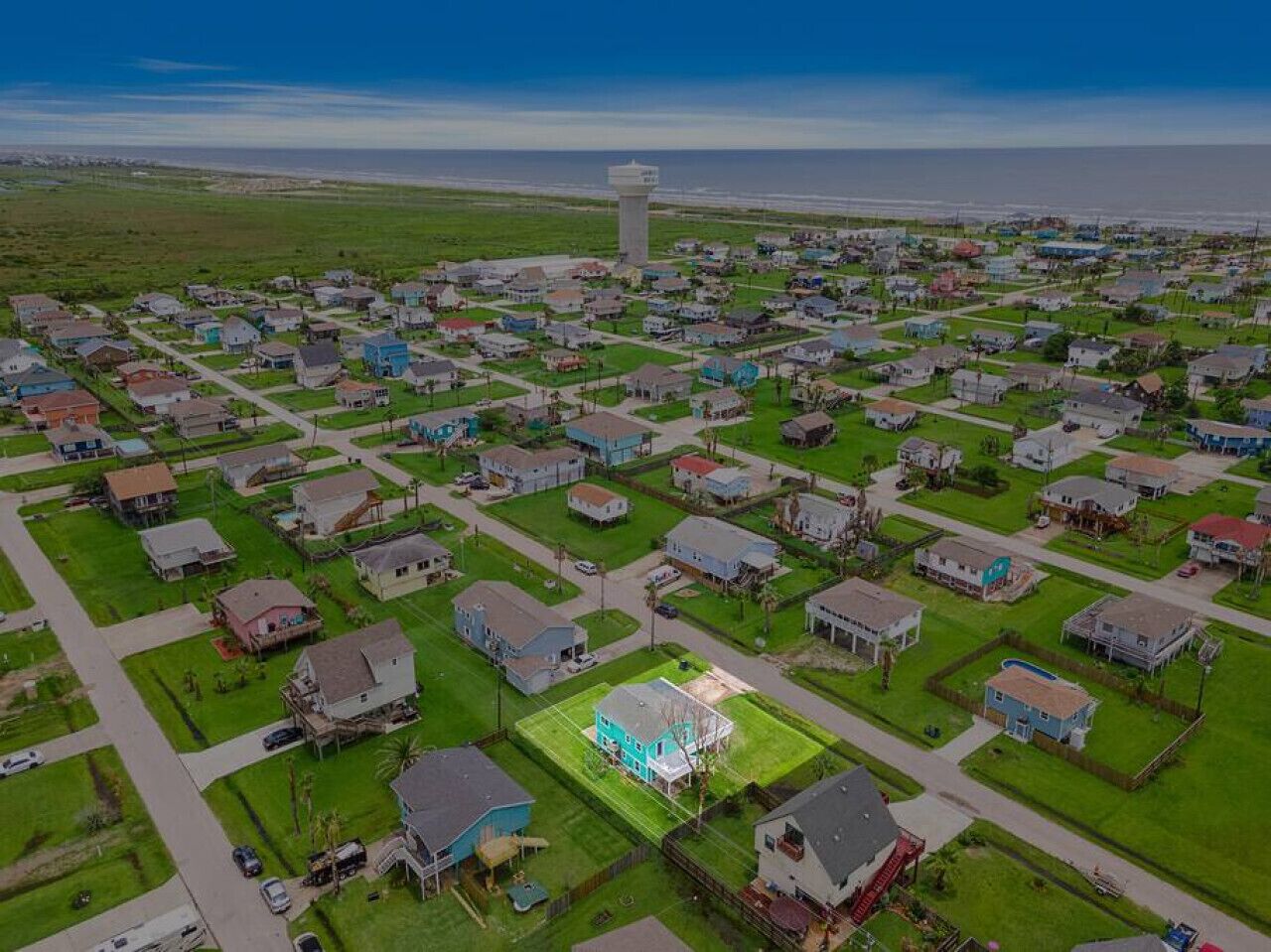 Una vista aerea di un quartiere residenziale con case, una torre d'acqua e cielo sereno.
