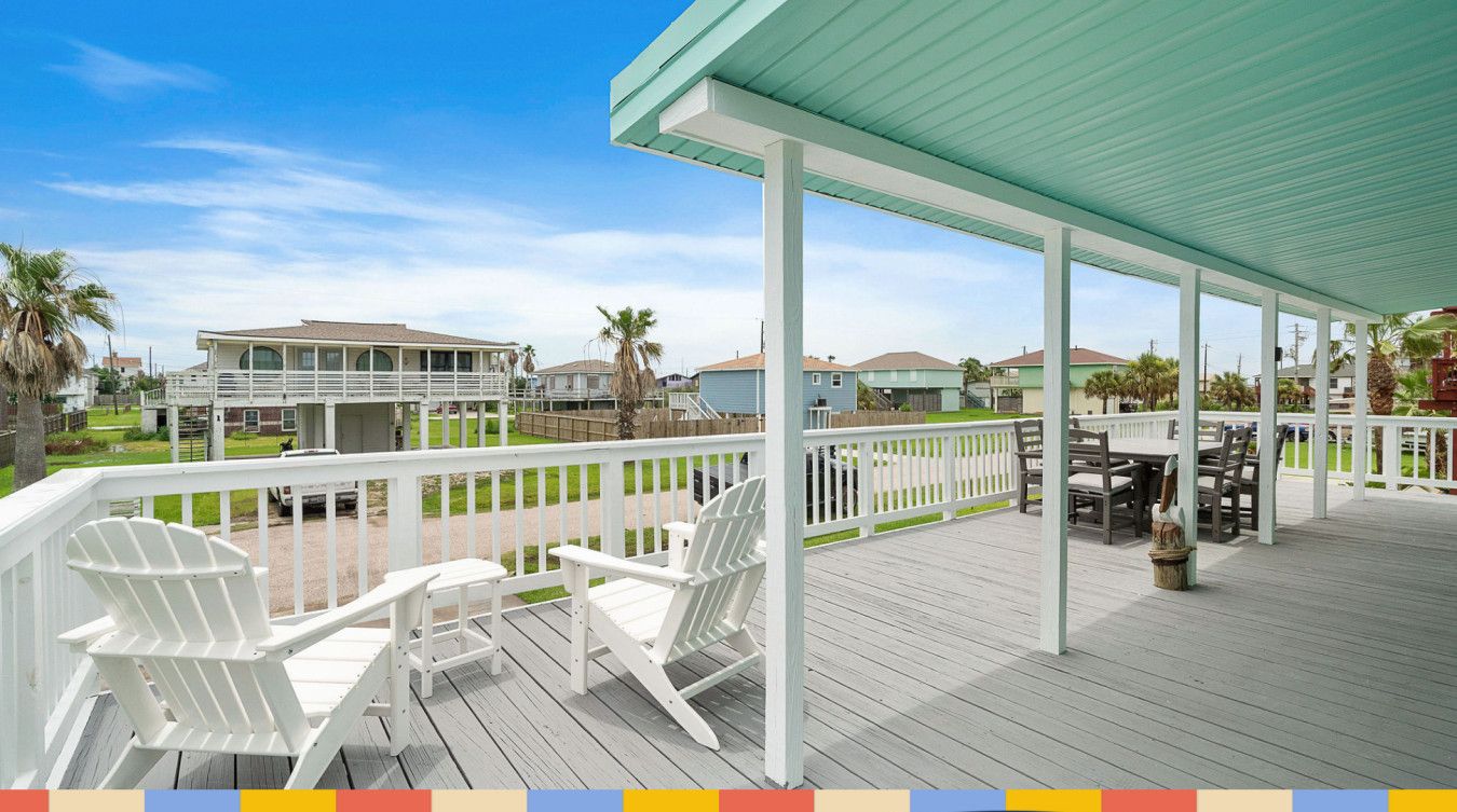 A covered deck with white Adirondack chairs, a table, and a potted plant.