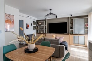 Een moderne woonkamer met een houten eettafel, groene stoelen, een grijze bank en een grote flatscreen televisie.