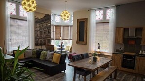 A modern living room with a dark sofa, wooden dining table, and a kitchen area with wooden cabinets and a stove. - Inviting 2-bed Apartment in Matlock Sleeps 6 (Matlock)