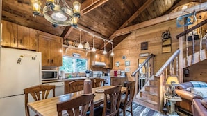 Interior de uma cabana de madeira com sala de jantar, cozinha e escada para um mezanino.