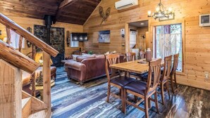 Interior acolhedor de uma cabana, com área de jantar de madeira, lareira e escada.