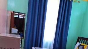 Ein Schlafzimmer mit Bett, Vorhängen, Schreibtisch und Fliesenboden.