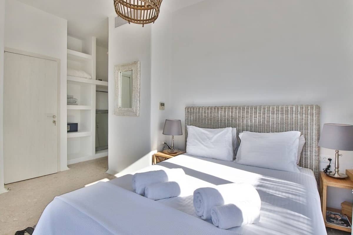 Habitación de hotel con una cama grande, dos lámparas de noche, cabecero de mimbre, armario y un espejo en la pared.