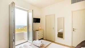 Un dormitorio con cama, cómoda, televisor y vista a la playa.