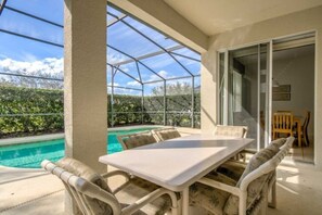 A covered patio with a pool, outdoor furniture, and a view of the surrounding greenery. - Beautiful Disney's pool villa (Davenport)