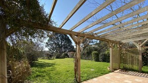 Een overdekt terras met betegelde vloer en een pergola van hout.